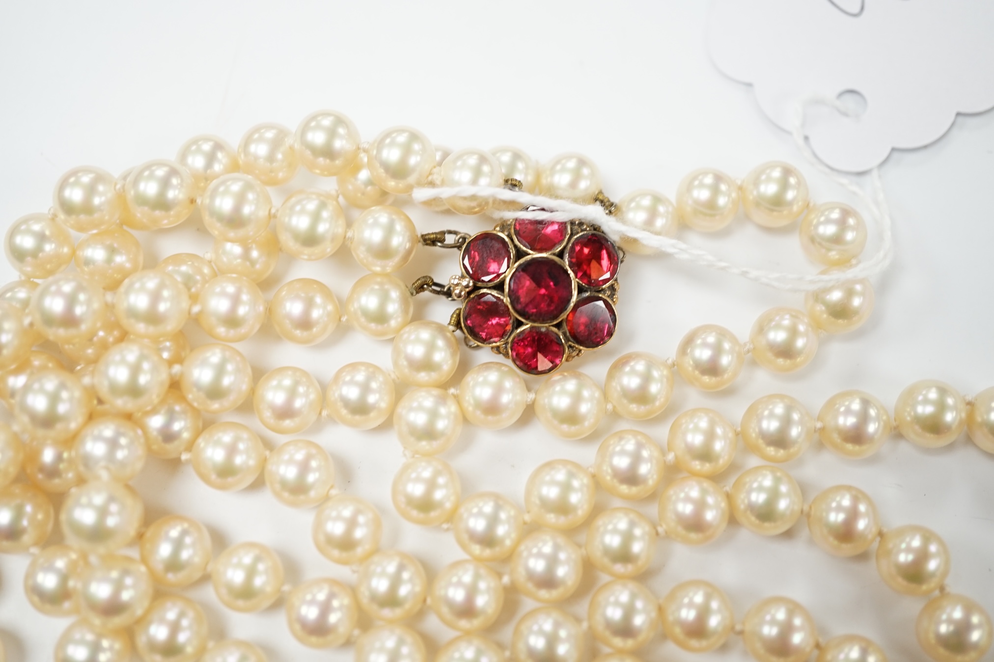 A late 1950's triple strand simulated pearl necklace, with garnet cluster set 9ct gold clasp, 66cm. Condition - fair